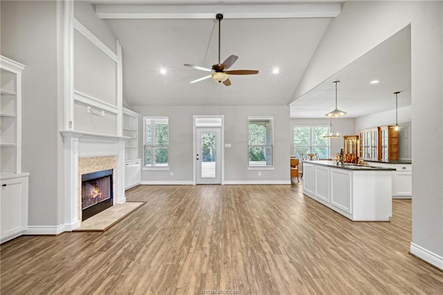 unfurnished living room with beamed ceiling, ceiling fan, and light wood-type flooring