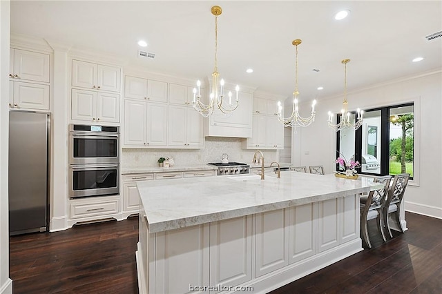 kitchen featuring a spacious island, hanging light fixtures, light stone countertops, white cabinetry, and stainless steel appliances