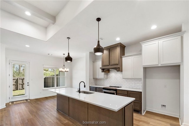 kitchen featuring backsplash, electric stove, sink, light hardwood / wood-style flooring, and decorative light fixtures