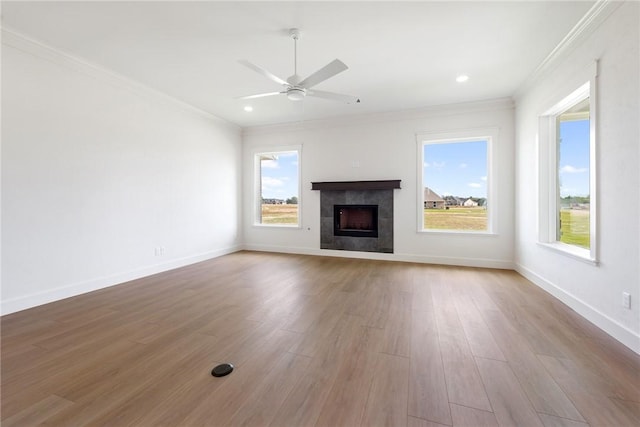 unfurnished living room with a healthy amount of sunlight, light wood-type flooring, crown molding, and a tile fireplace