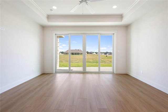 spare room featuring a tray ceiling, crown molding, ceiling fan, and light hardwood / wood-style floors