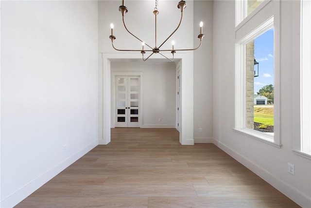 unfurnished dining area with french doors, light hardwood / wood-style floors, and a notable chandelier