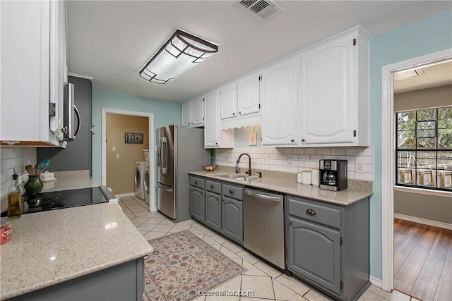 kitchen featuring washer and dryer, appliances with stainless steel finishes, gray cabinets, and white cabinetry