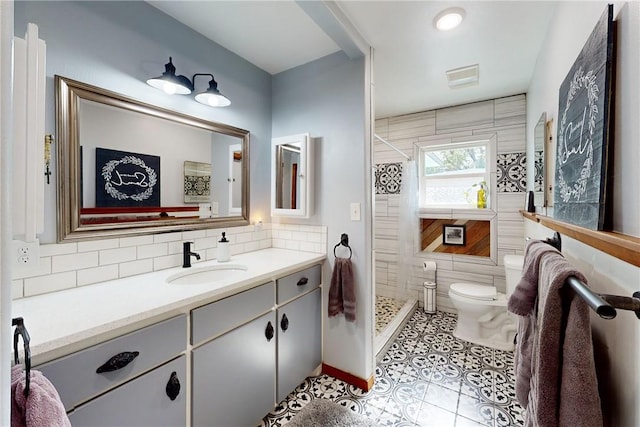 bathroom with tile patterned flooring, toilet, tiled shower, vanity, and tile walls