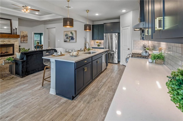 kitchen with backsplash, sink, light hardwood / wood-style flooring, appliances with stainless steel finishes, and decorative light fixtures