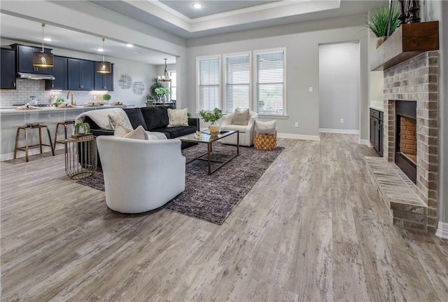 living room featuring a raised ceiling, a fireplace, light hardwood / wood-style floors, and ornamental molding