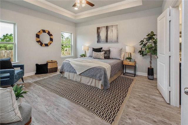 bedroom featuring a tray ceiling, light hardwood / wood-style flooring, ceiling fan, and crown molding