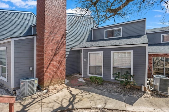 exterior space featuring central AC, a chimney, and a shingled roof