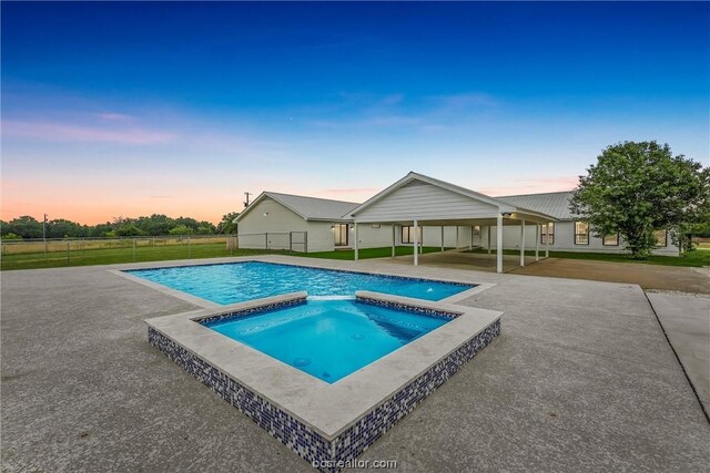 pool at dusk featuring an in ground hot tub and a patio