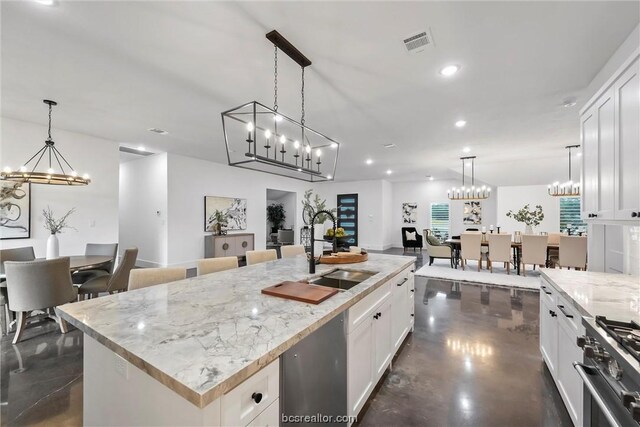 kitchen featuring stainless steel appliances, sink, pendant lighting, white cabinetry, and an island with sink