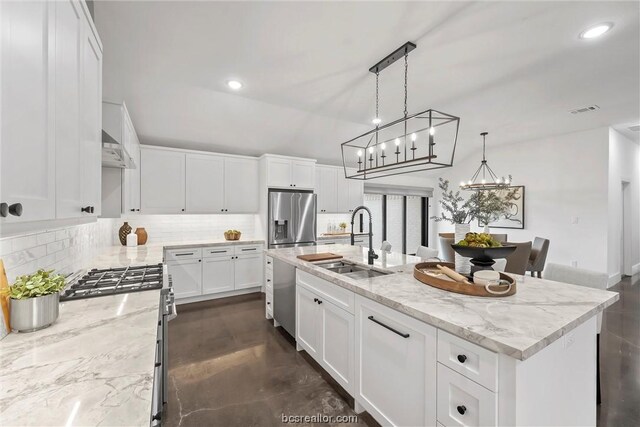 kitchen with light stone countertops, stainless steel appliances, sink, white cabinetry, and an island with sink