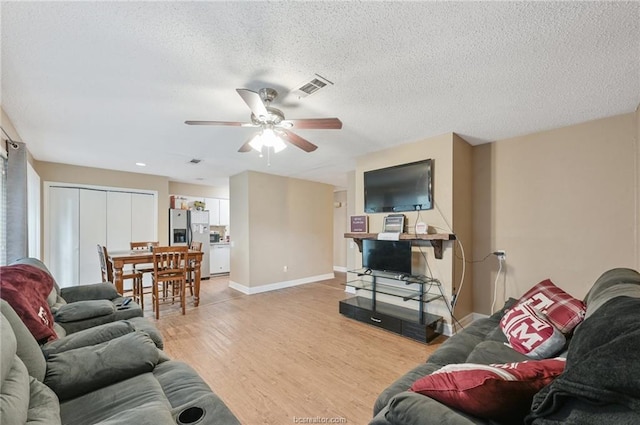 living area featuring light wood-type flooring, visible vents, a textured ceiling, baseboards, and ceiling fan