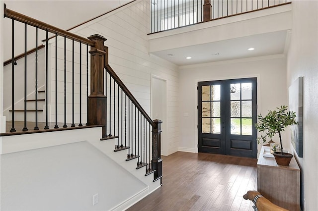 foyer featuring french doors, a towering ceiling, ornamental molding, dark wood-type flooring, and wood walls