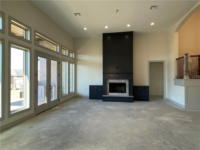 unfurnished living room featuring a towering ceiling, a large fireplace, plenty of natural light, and visible vents