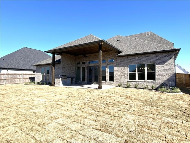 rear view of property featuring a patio, brick siding, fence, a lawn, and roof with shingles