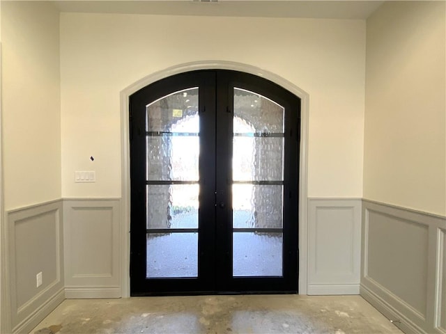 doorway featuring french doors, unfinished concrete flooring, and a decorative wall