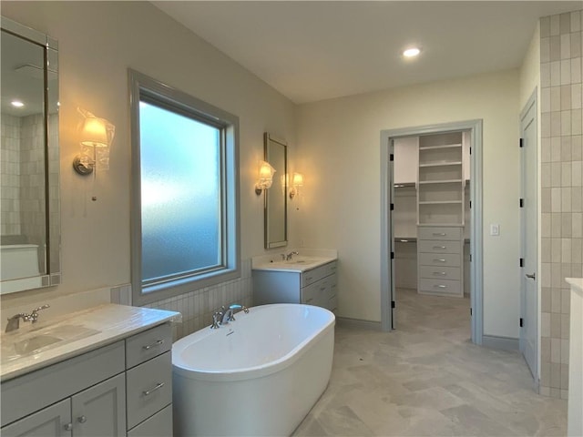 bathroom with a freestanding tub, two vanities, a sink, and a spacious closet