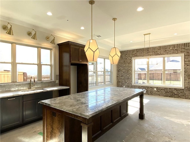 kitchen featuring dark brown cabinetry, brick wall, a sink, a center island, and decorative light fixtures