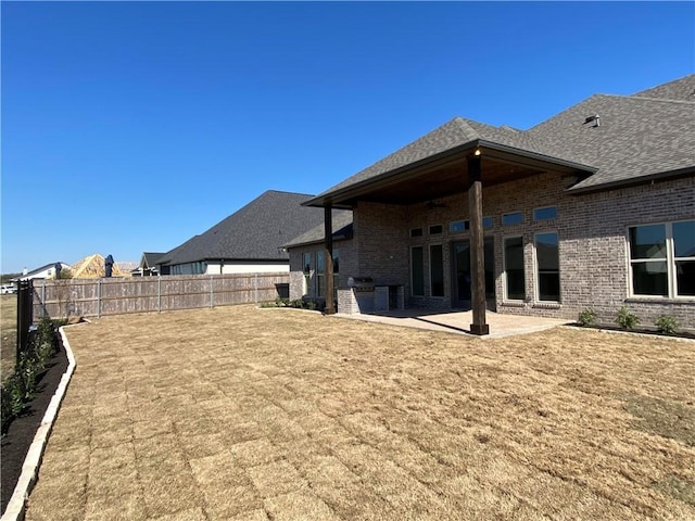 back of property featuring a fenced backyard, brick siding, a shingled roof, a lawn, and a patio area