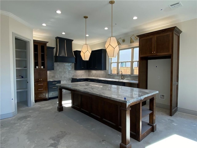 kitchen with glass insert cabinets, decorative light fixtures, a center island, light stone countertops, and premium range hood