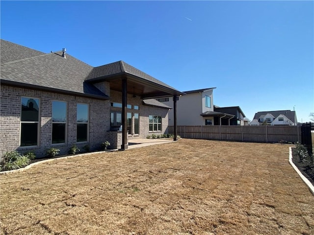 back of property featuring a yard, brick siding, fence, and roof with shingles