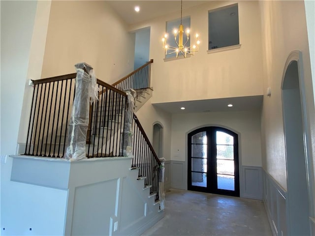 entryway with arched walkways, wainscoting, stairs, french doors, and a decorative wall