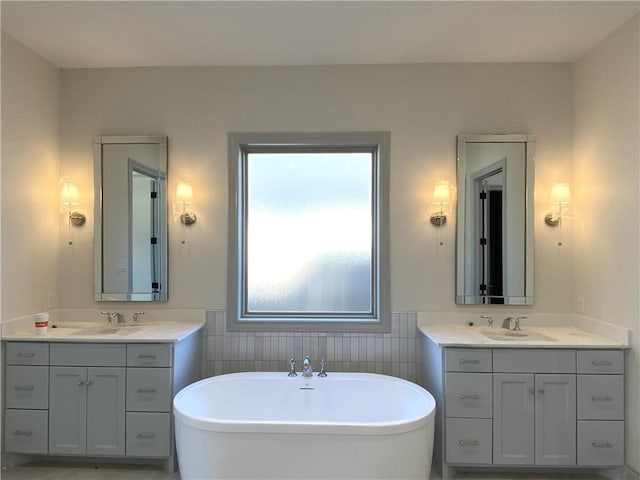 full bathroom featuring a soaking tub, two vanities, a sink, and tile walls