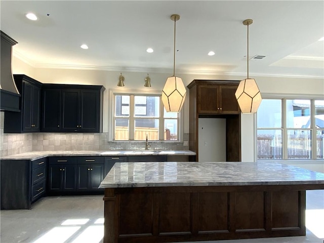 kitchen with hanging light fixtures, light stone counters, decorative backsplash, and a sink