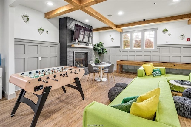 recreation room featuring beamed ceiling, a fireplace, and light hardwood / wood-style floors