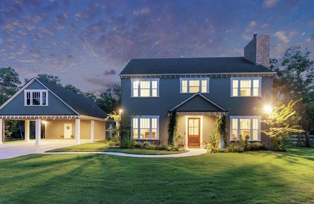 colonial home with a lawn, a carport, a chimney, and concrete driveway