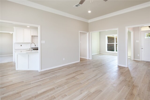 unfurnished living room with ceiling fan, sink, crown molding, and light wood-type flooring