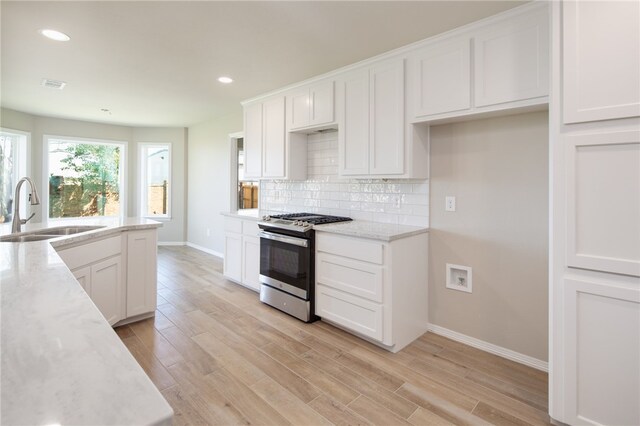 kitchen featuring light wood-type flooring, backsplash, sink, white cabinets, and stainless steel gas stove