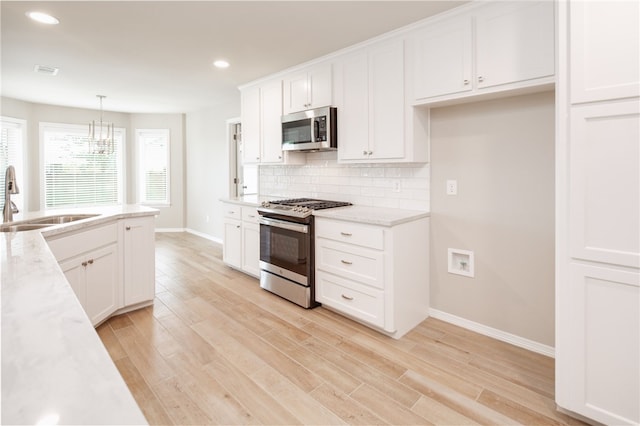 kitchen featuring light wood finished floors, backsplash, a sink, baseboards, and appliances with stainless steel finishes