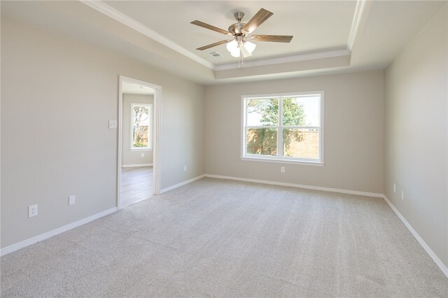 carpeted empty room with a raised ceiling, ceiling fan, and ornamental molding