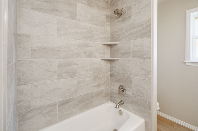 bathroom with hardwood / wood-style floors, toilet, and tiled shower / bath