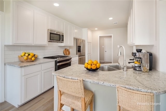 kitchen with light wood-style flooring, a peninsula, tasteful backsplash, appliances with stainless steel finishes, and white cabinetry