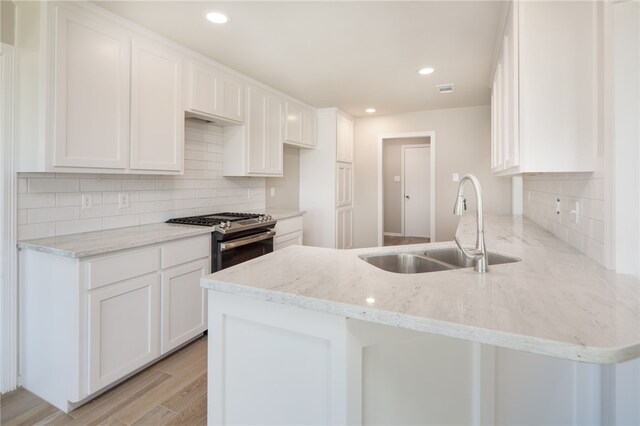 kitchen with sink, stainless steel range with gas cooktop, kitchen peninsula, light hardwood / wood-style floors, and white cabinets