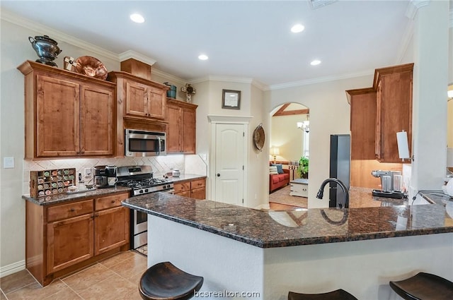 kitchen with kitchen peninsula, appliances with stainless steel finishes, dark stone counters, and a breakfast bar area