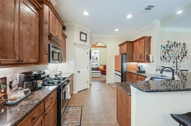 kitchen with crown molding, dark stone countertops, sink, and stainless steel appliances