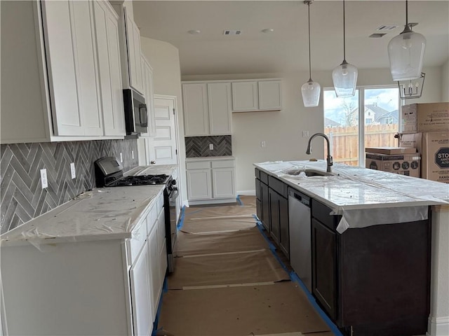 kitchen with decorative light fixtures, stainless steel appliances, white cabinetry, and an island with sink