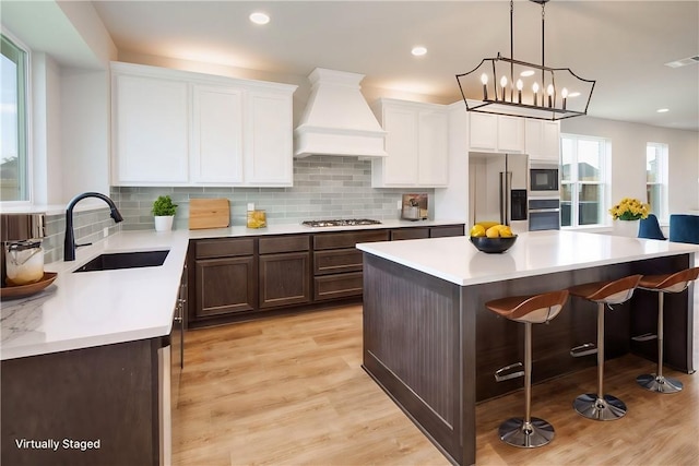 kitchen with sink, a center island, a notable chandelier, custom range hood, and appliances with stainless steel finishes