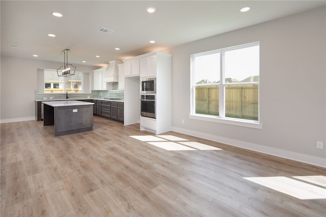 kitchen featuring backsplash, stainless steel oven, a center island, white cabinetry, and hanging light fixtures