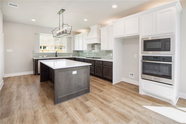 kitchen with appliances with stainless steel finishes, custom exhaust hood, sink, white cabinets, and a kitchen island