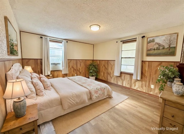 bedroom featuring a textured ceiling, wood finished floors, wood walls, and wainscoting