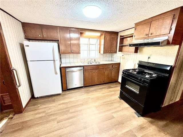 kitchen with wallpapered walls, under cabinet range hood, freestanding refrigerator, black range with gas cooktop, and stainless steel dishwasher