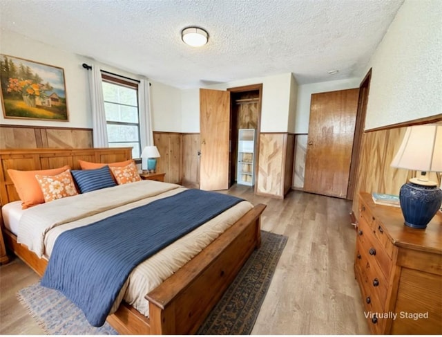 bedroom featuring light wood finished floors, wooden walls, wainscoting, a closet, and a textured ceiling