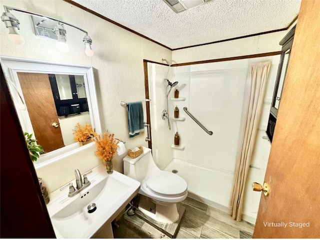 full bathroom featuring toilet, a stall shower, a textured wall, a textured ceiling, and a sink