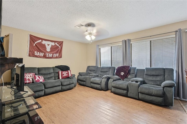 living area featuring a ceiling fan, a textured ceiling, visible vents, and wood finished floors