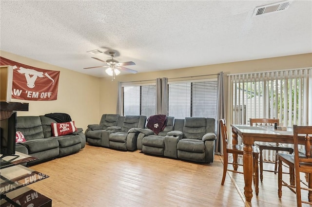 living room with a textured ceiling, light wood-type flooring, and ceiling fan