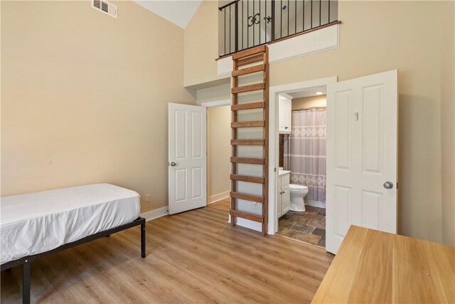 bedroom featuring hardwood / wood-style flooring, high vaulted ceiling, and ensuite bath